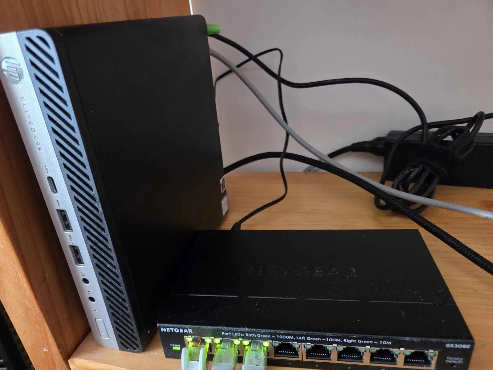 El mini PC HP EliteDesk de pie en una balda, junto al switch Netgear de 8 puertos con tres cables de red conectados y sus luces encendidas.